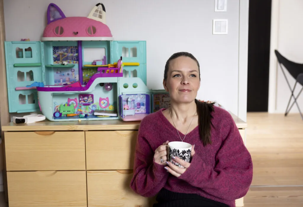 Valeäiti-bloggaaja Hanne Kettunen istuu kahvikuppi kädessään lapsen lelu taustalla.