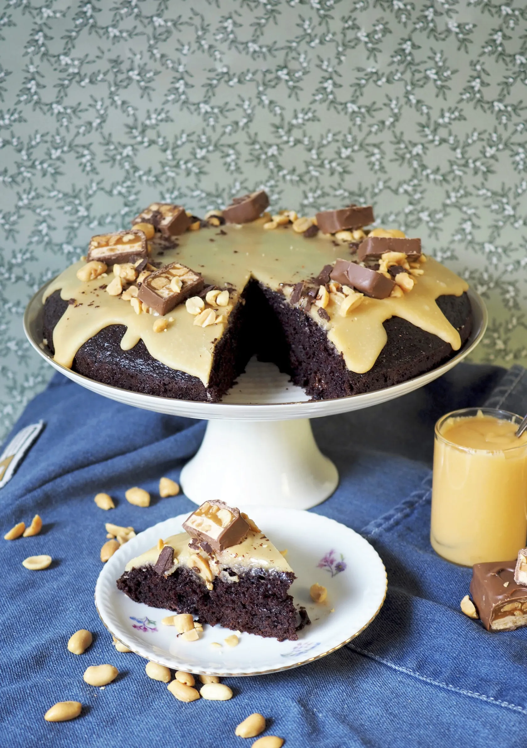 Snickers-kakku, jostta leikattu pala lautaselle. Päällä kakussa on koristeena suklaapatukan paloja. 