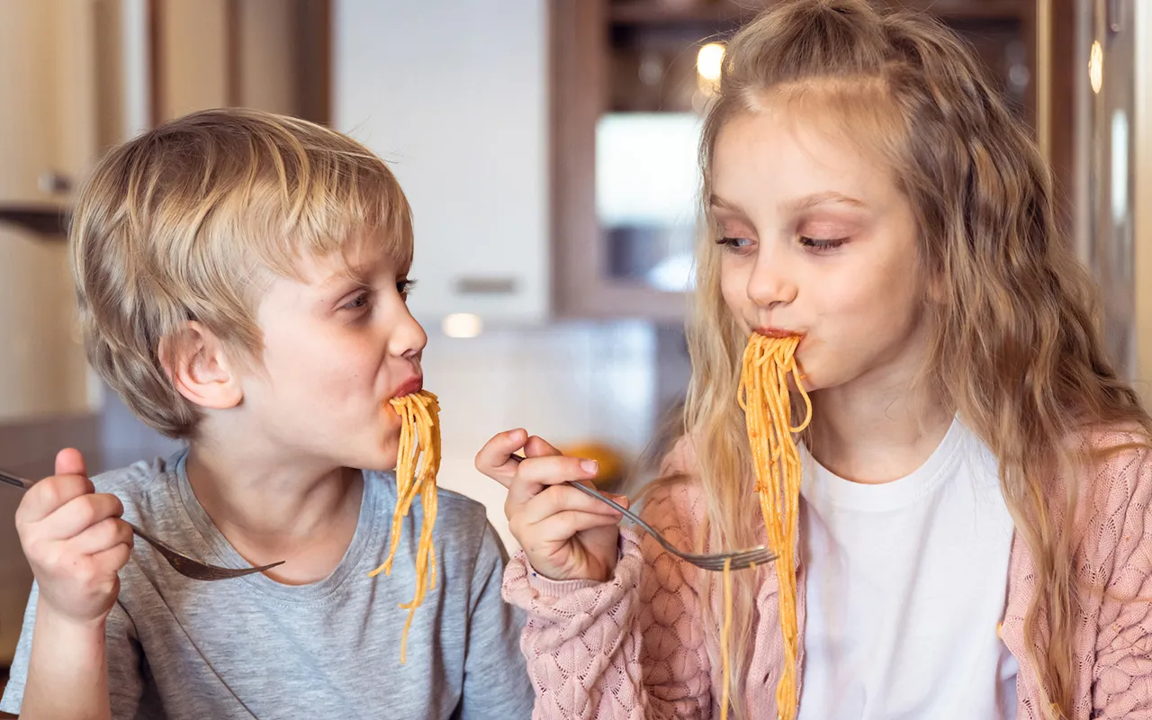 Lapset syövät spagettia.