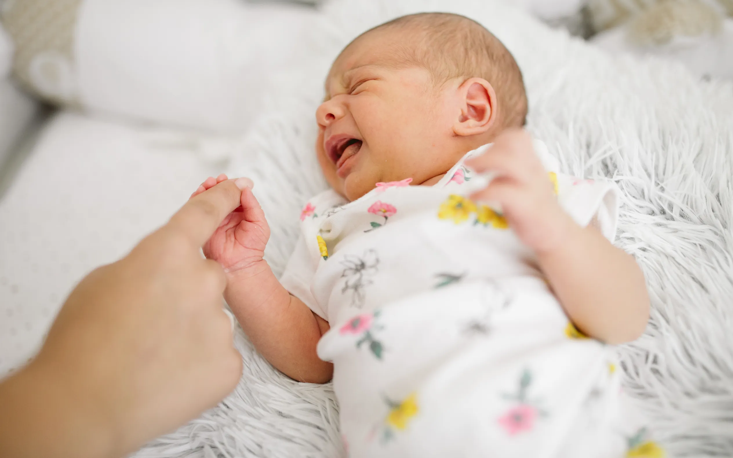 Vauva makoilee ja itkee pitäen vanhemman kädestä kiinni.